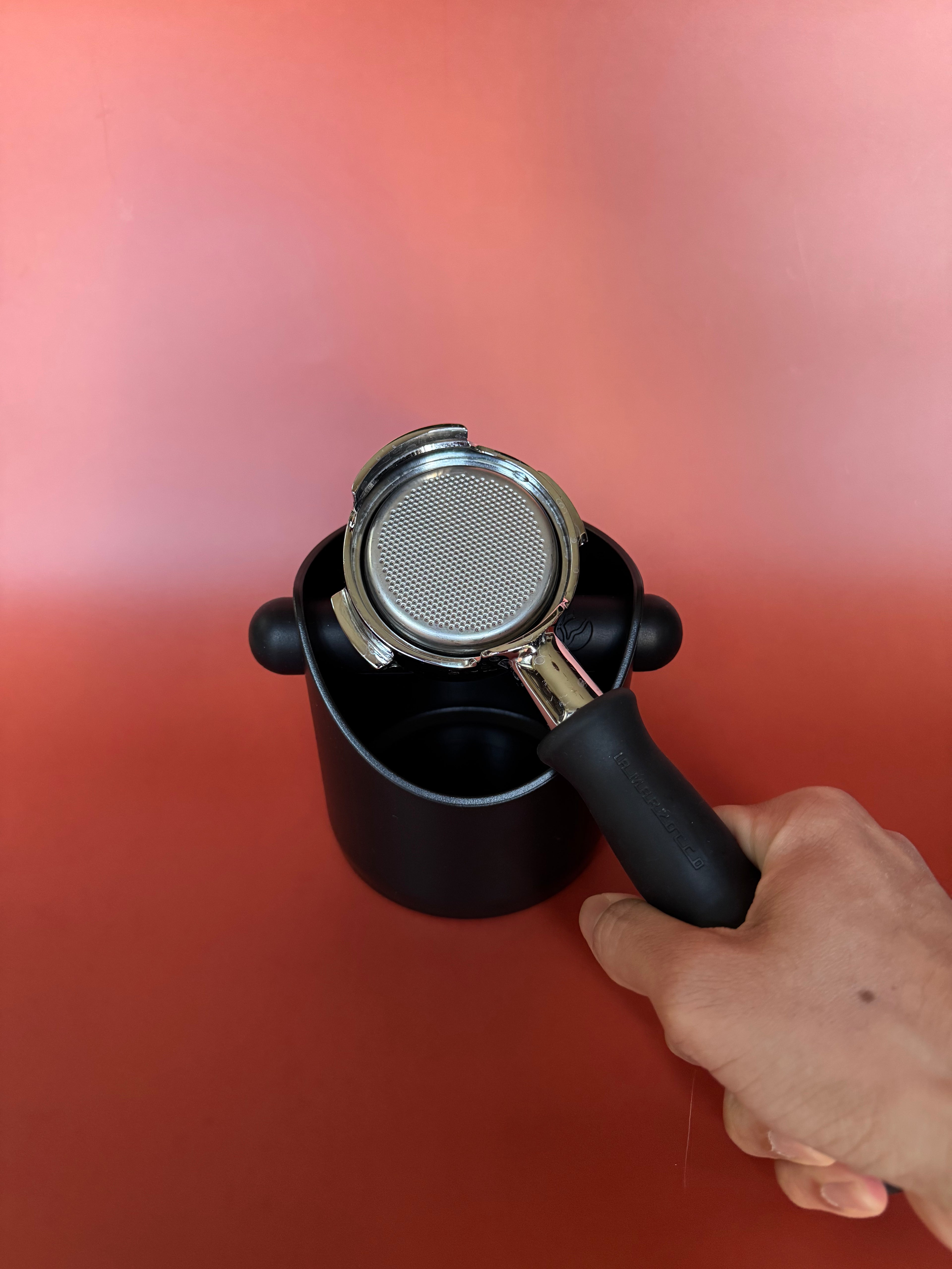 Black coffee filter with metal mesh held by a hand against a blakc knockbox